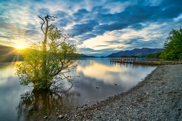 Sunset with dramatic clouds and wooden jetty at Derwentwater Lake in the Lake District, UK.