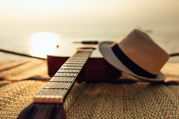 Guitar and hat on reed mat near the sea at sunset. Travel, vocation, holiday, summer concept.