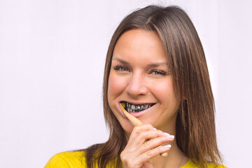 Close-up of happy woman brushing teeth with eco friendly bamboo toothbrush with black charcoal whitening toothpaste.