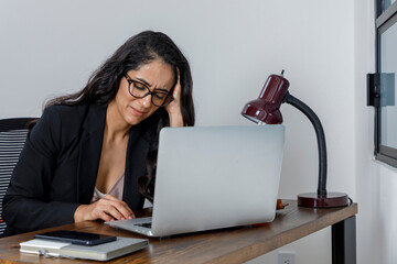 Mujer ejecutiva cansada por el exceso de trabajo en casa, se lleva las manos a la cabeza frente a...