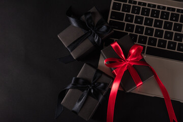 Black Friday sale online shopping commerce, Top view of gift box wrapped black paper and red bow ribbon present on a laptop computer keyboard, studio shot on black background