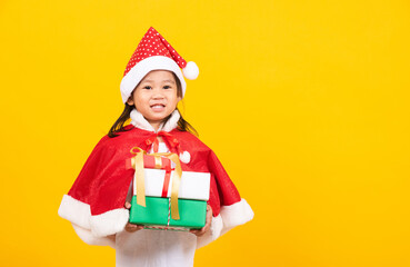 Asian little cute girl smile and excited, Kid dressed in red Santa Claus hat hold gift box on hands concept of holiday Christmas Xmas day or Happy new year, studio shot isolated on yellow background