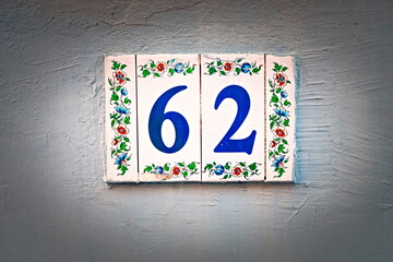 62, number sixty-two, blue digits on floral tiles, vignetted.