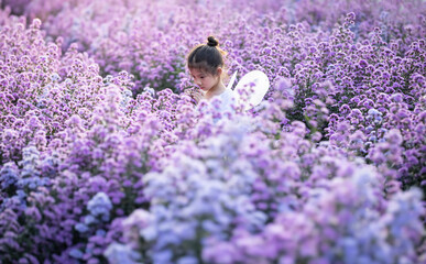 Cute little girl smelling flowers and wear a magic ballet fairy costume in beautiful purple of...