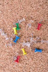 Scattered pile of multicolored thumb tacks on a brown cork board