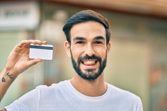 Young hispanic man smiling happy holding credit card at the city.