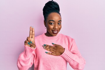 Young african american woman wearing casual winter sweater smiling swearing with hand on chest and...