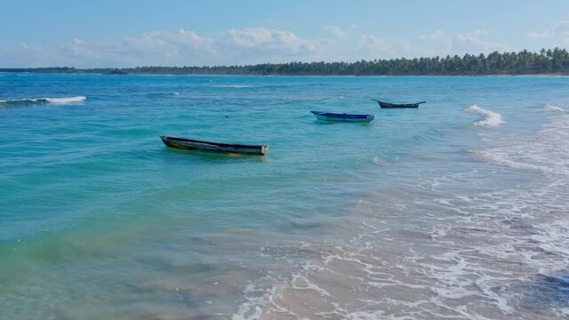 Aerial drone shot of three fishing boats, waves on the turquoise blue beach, radiant sun