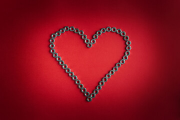 Heart made of metal nuts on a bright red background. Valentine's day symbol