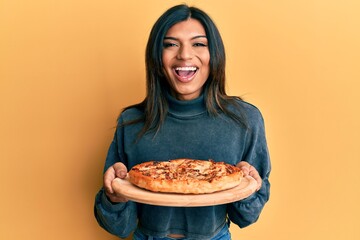 Young latin transsexual transgender woman holding italian pizza smiling and laughing hard out loud because funny crazy joke.