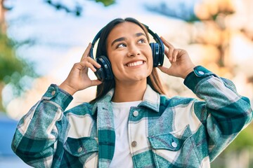 Young latin girl smiling happy using headphones at the city.