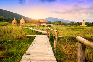 autumn sunrise in mountainous rural area. Bamboo Walkway and cottage in golden foliage on the meadow in weathered grass
