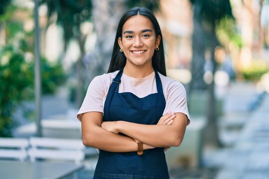 Young latin barista girl with arms crossed smiling happy at the coffee shop