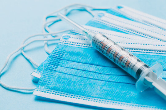 One hundred US dollars inside of a syringe that is sitting on top of some blue face masks 