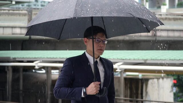 Portrait of Confidence Asian businessman office worker in suit holding black umbrella standing in the rain. Handsome man business people working in city office district in bad weather raining day.