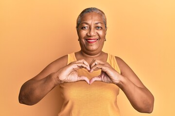 Senior african american woman wearing casual style with sleeveless shirt smiling in love doing heart symbol shape with hands. romantic concept. - Powered by Adobe