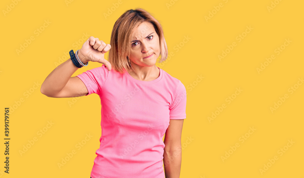 Sticker Young blonde woman wearing sportswear looking unhappy and angry showing rejection and negative with thumbs down gesture. bad expression.