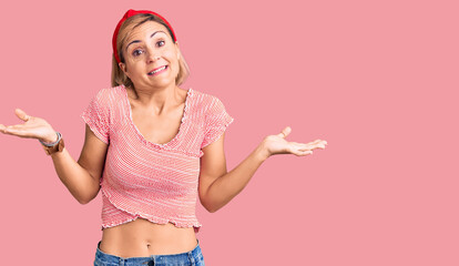 Young blonde woman wearing casual clothes and diadem clueless and confused expression with arms and...