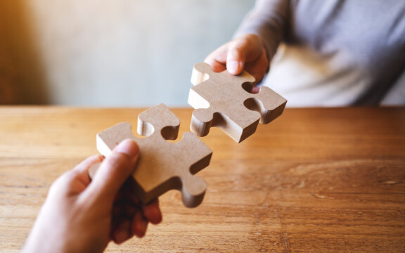 Closeup image of two people holding and putting a piece of wooden jigsaw puzzle together