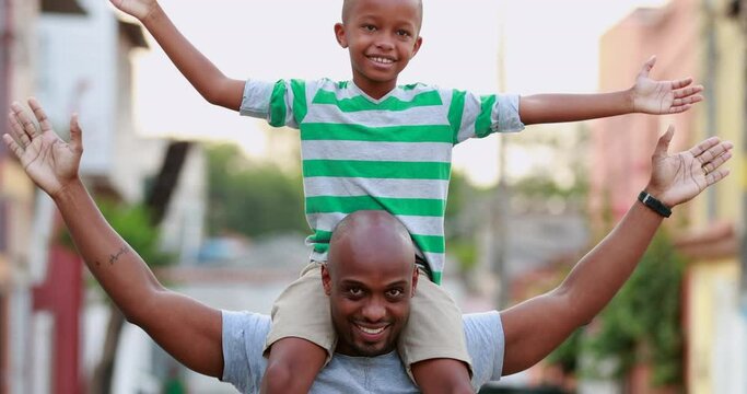 Son on top of father shoulders outside. African black parent and child bonding together outdoors