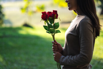Closeup image of a beautiful asian woman holding red roses flower in the park