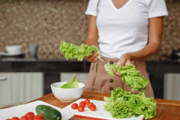 Cropped image unrecognisable woman cooking healthy food at home kitchen - lettuce salad, cherry tomatoes and cucumber