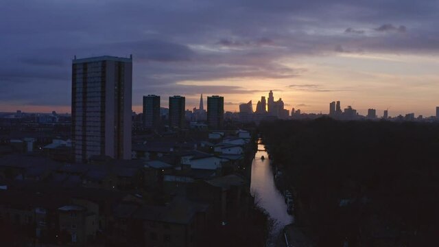 Low dolly back Aerial drone shot of house boat on London Canal Victoria park towards city skyline to highway at sunset