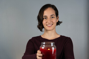 Mujer joven mirando sonreida sosteniendo una vela encendida color roja
