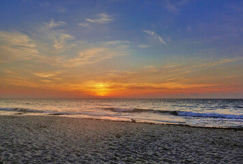 Beautiful sunrise over the Caribbean Sea. The blue sky is highlighted in orange at the horizon. Light clouds. Turquoise waves roll with foam on the sandy beach.