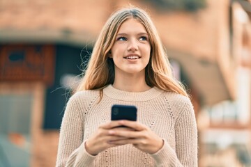 Beautiful caucasian teenager smiling happy using smartphone at the city.