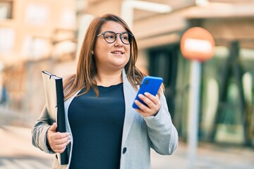 Young plus size businesswoman using smartphone holding binder at the city