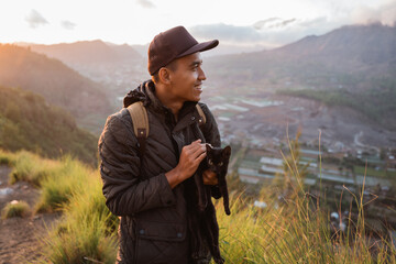 Portrait adventurous man with a backpack captures the moment with cat. Beautiful mountain scenery...