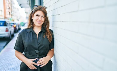 Young hispanic woman smiling happy leaning on the wall at street of city