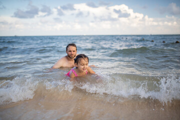 Happy father and young daughter playing in the water at the beach