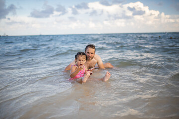 Naklejka premium Happy father and young daughter playing in the water at the beach