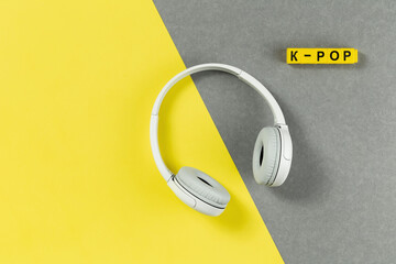 Wireless funky modern gray headphones on illuminating yellow and grey background. Remote learning or listening to music or radio. Trendy lifestyle concept with copy space. K-pop text music
