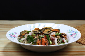 Spicy vermicelli salad mixed with steamed mussel, chilly and sliced shallot on the plate. Famous traditional appetizer menu in Asia restaurant. 