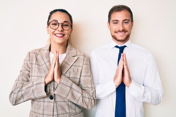 Beautiful couple wearing business clothes praying with hands together asking for forgiveness smiling confident.