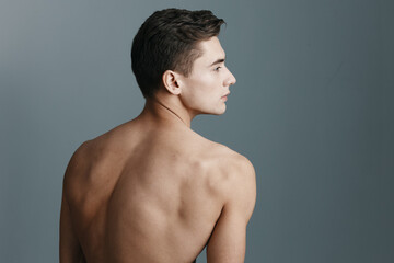 Rear view of a sexy man with a naked back looks to the side on a gray background