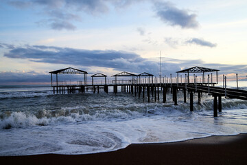 View from beach to water of sea, waves with white foam, pierce and sky with clouds in a nice evening.