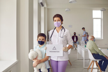 Obraz premium Young nurse in protective mask and little girl standing with sign vaccination