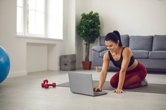 Woman Sitting On Sports Mat At Home, Shopping For Sportswear Online Or Watching Video Workout Lesson