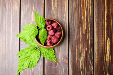 Fresh raspberry red berries with green leaves in bowl on wooden table