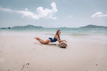 Young attractive blonde woman in a blue swimming suit lying on a sandy beach against the sea background. Summer vacation concept