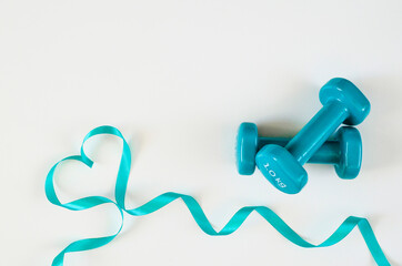 Two turquoise dumbbells with heart from ribbon on white background with copy space. Concept of Valentines day, love, healthy lifestyle, giving gifts, love of sports. Trendy color green tide.