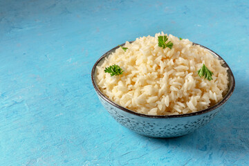 A bowl of rice, served with fresh parsley leaves, on a blue background with a place for text