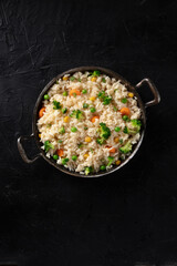 Vegetable rice with broccoli, carrot and grean peas, overhead shot on a black background with a place for text