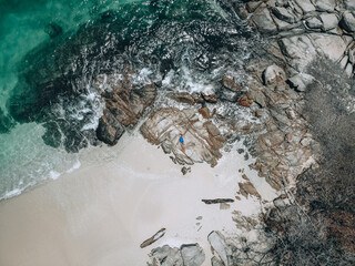 From above photo of a pretty young woman in a blue swimming suit lying on the rock in high tide. Summer vacation concept