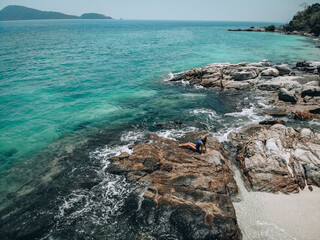 Pretty young woman in a blue swimming suit sunbathing on the rocks in high tide. Summer vacation concept