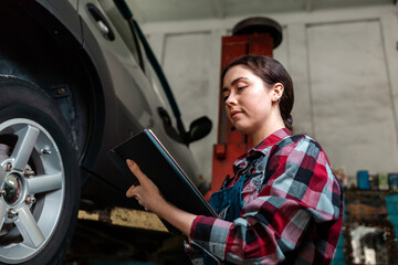 A young Caucasian female mechanic, in uniform, with a tablet in her hands. Car on the lift. Modern car diagnostics. Bottom view